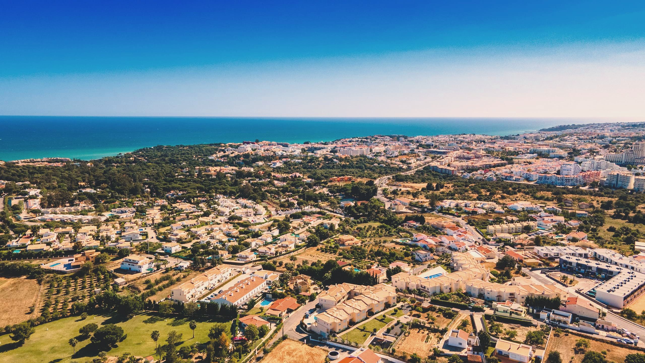Luftaufnahme über Balaia zur Küste von Albufeira, mit dem Grün von Balaia Golf, niedrigen Wohnstraßen und dem Atlantik dahinter
