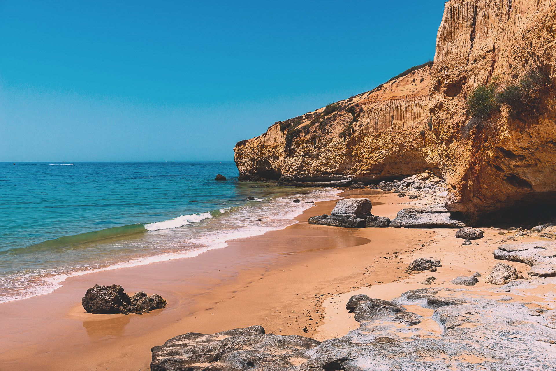 Ein ruhiger Strand bei Albufeira mit verstreuten Felsen unter hohen goldenen Klippen