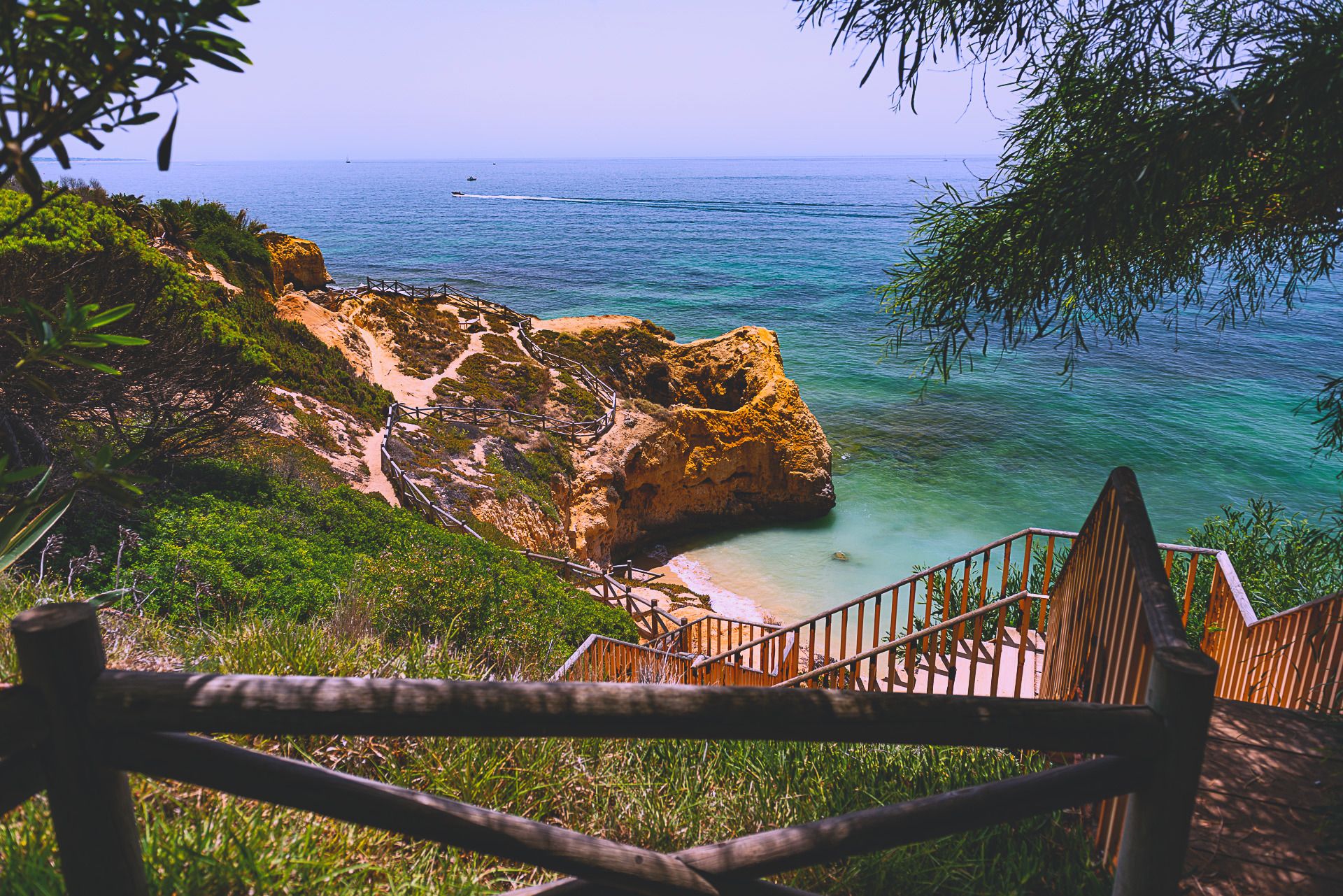 Ein hölzerner Bohlenweg, der sich zwischen goldenen Klippen zu einem Strand bei Albufeira hinunterschlängelt