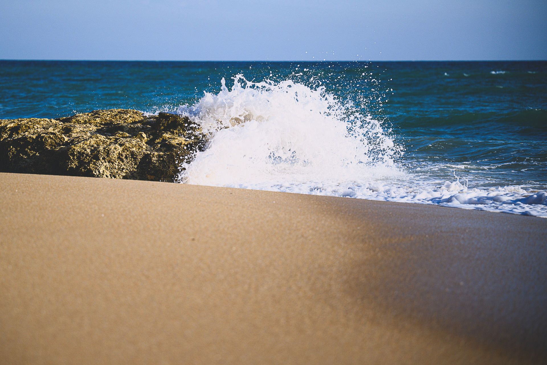 Eine Welle, die unter tiefblauem Himmel gegen eine Sandkante bricht
