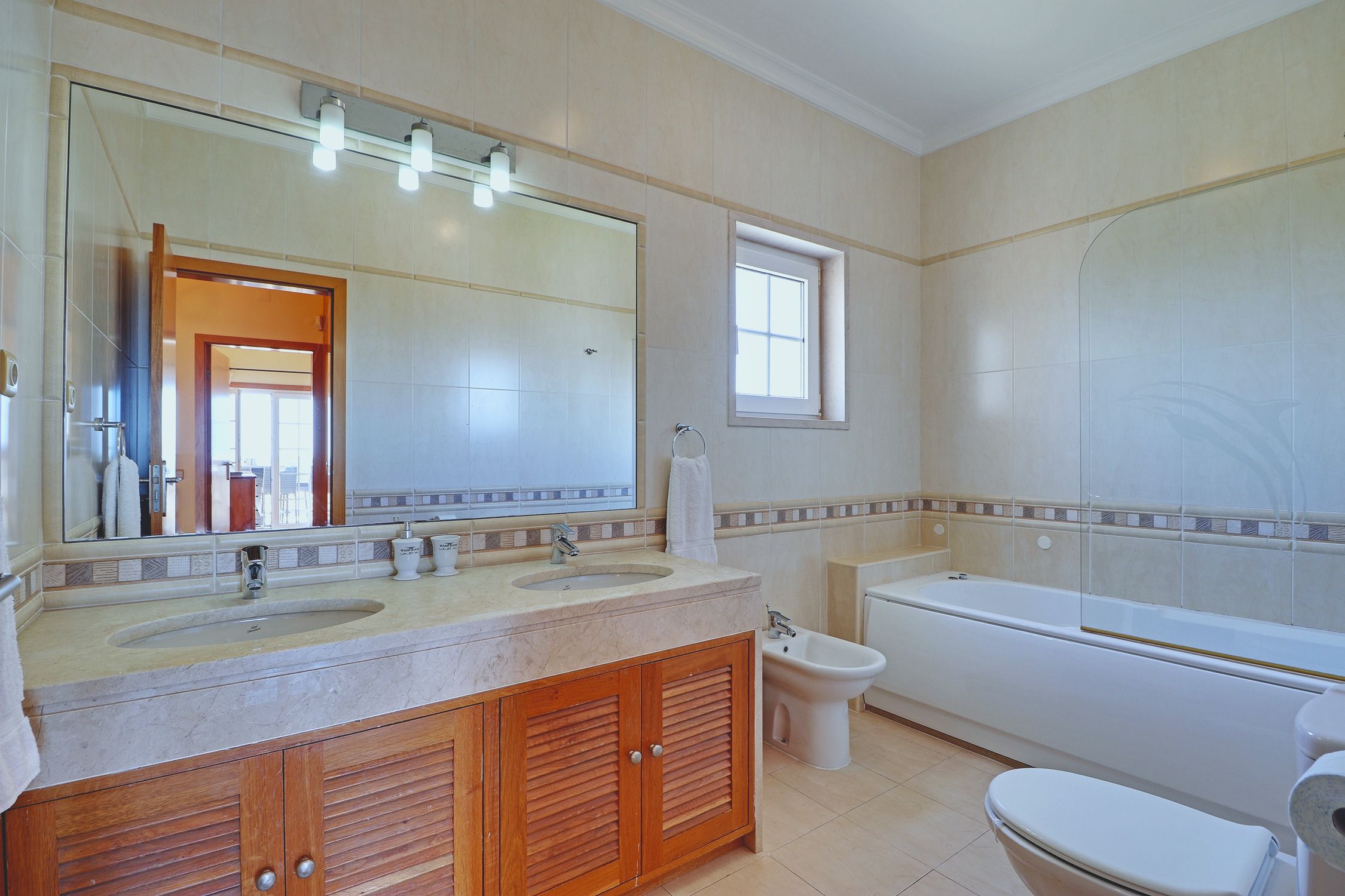 Ein Badezimmer mit Badewanne, Bidet, hölzernem Waschtisch und breitem Spiegel über dem Becken