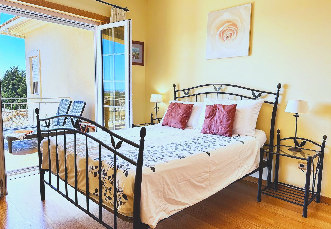 Ein Schlafzimmer mit Doppelbett und geöffneter Balkontür, mit schmiedeeisernem Bettgestell und Nachttischen