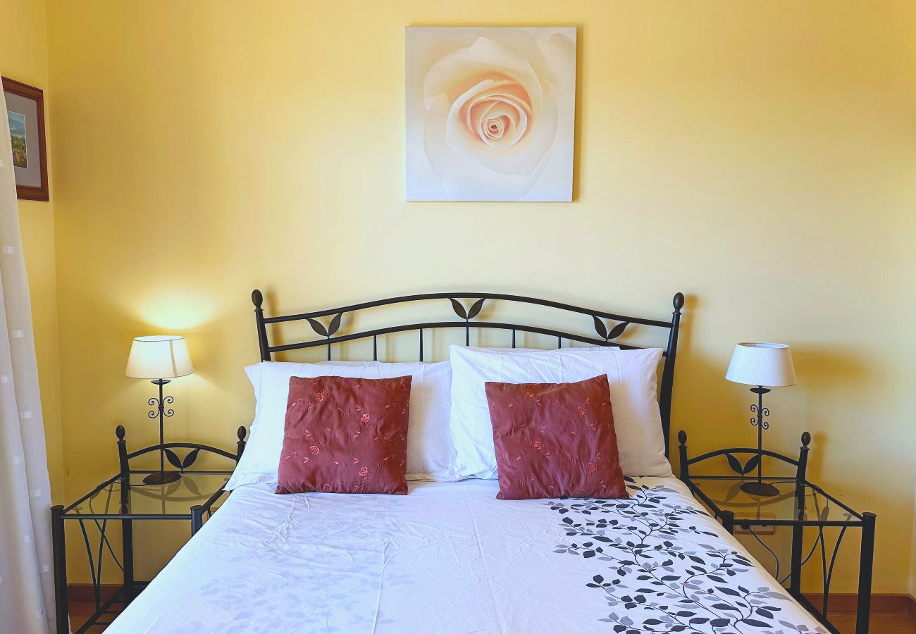 Ein Schlafzimmer mit Doppelbett mit schmiedeeisernem Gestell, Nachttischlampen und einem gerahmten Druck über dem Kopfende