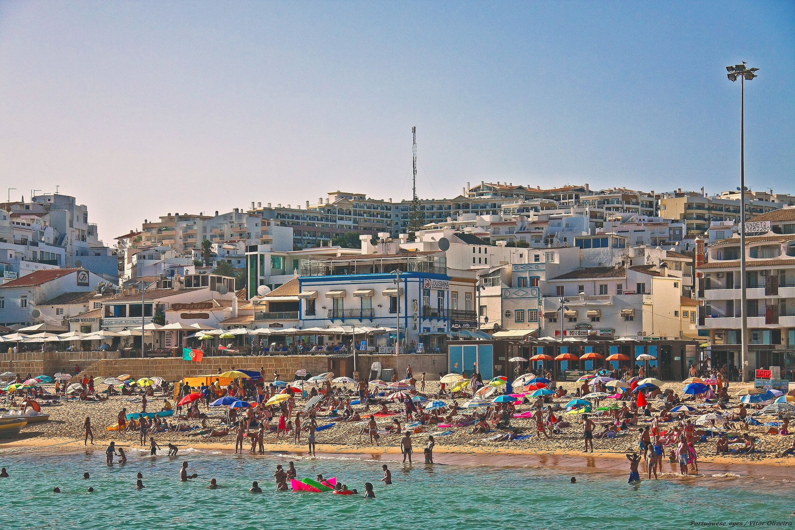 Praia dos Pescadores in der Altstadt von Albufeira an einem Sommertag, mit Sonnenschirmen am Strand und der weißen Stadt dahinter