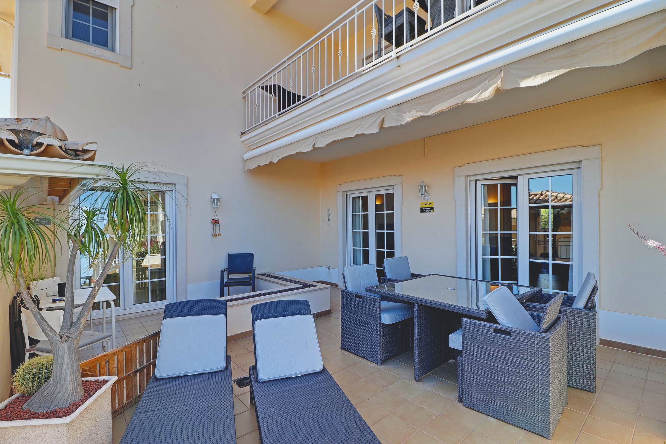 Terrasse im Erdgeschoss mit zwei Sonnenliegen und einer Rattan-Essgruppe, im Schatten der Markise unter dem Balkon